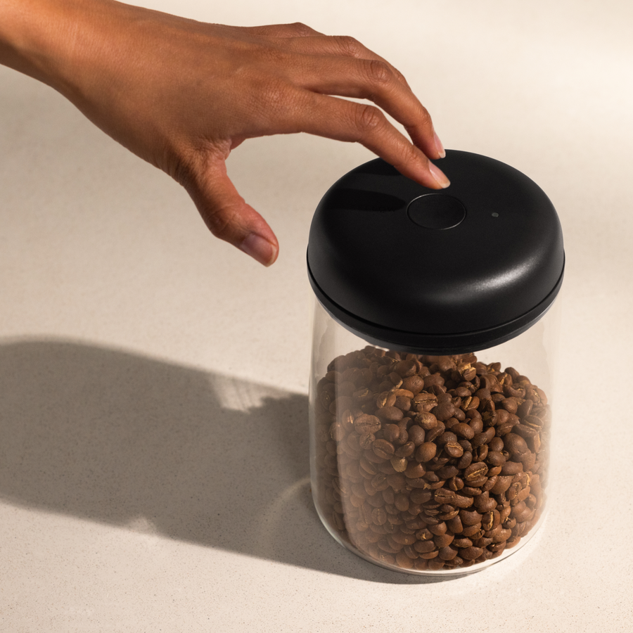 A person holds their finger on the vacuum seal button on a coffee bean canister