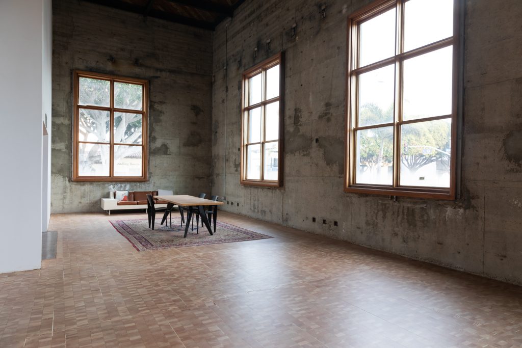 An interior view of the old Santa Monica post office, showing a table and chairs in front of three large windows