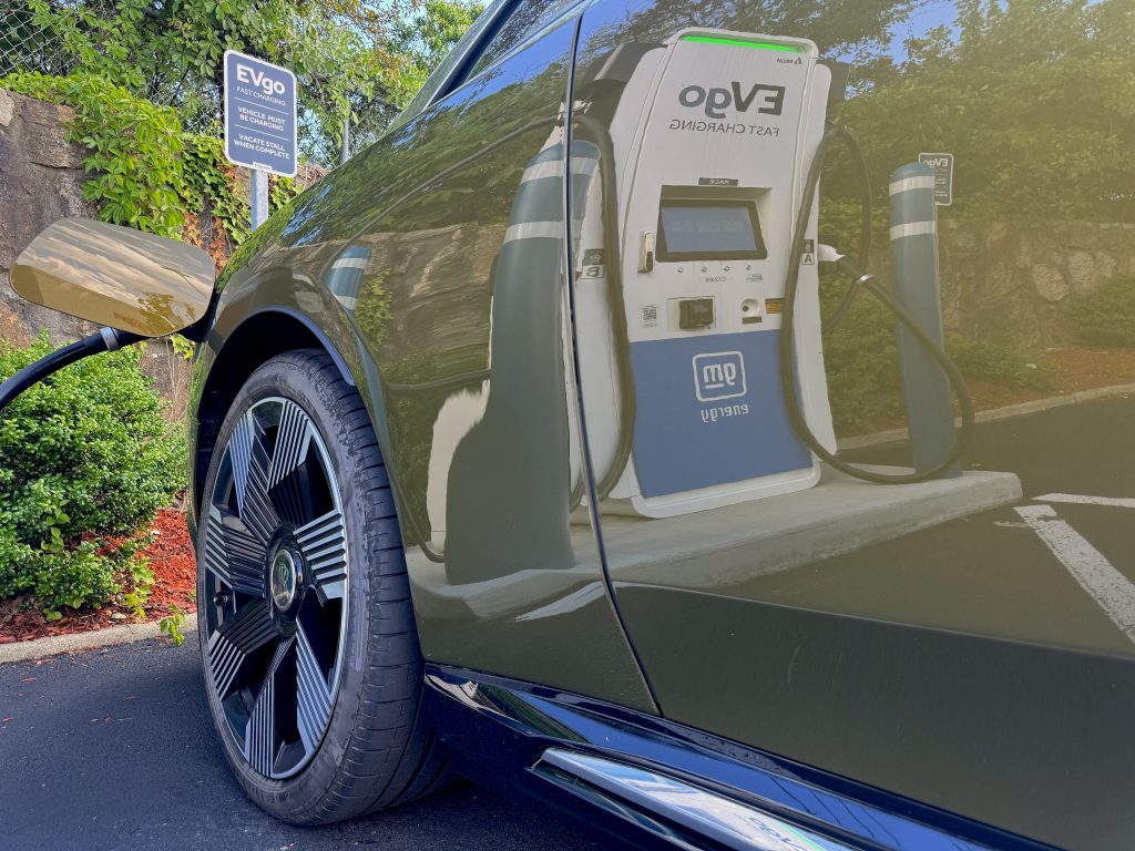 Olive green Rolls Royce Spectre parked at an EVgo charging station and plugged in