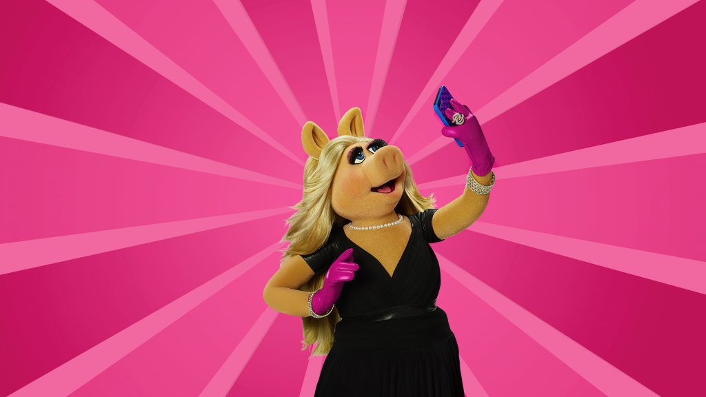 An image of Miss Piggy holding a phone, wearing pink gloves and a black dress, on a pink background